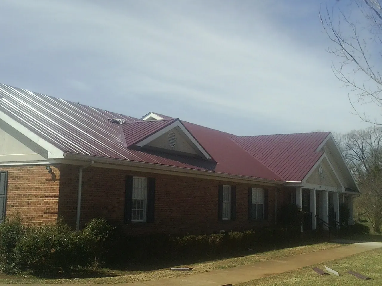 Red metal roof with gabled entries on a long brick building, from a Hail Damage Roof Repair job in Hurricane Mills