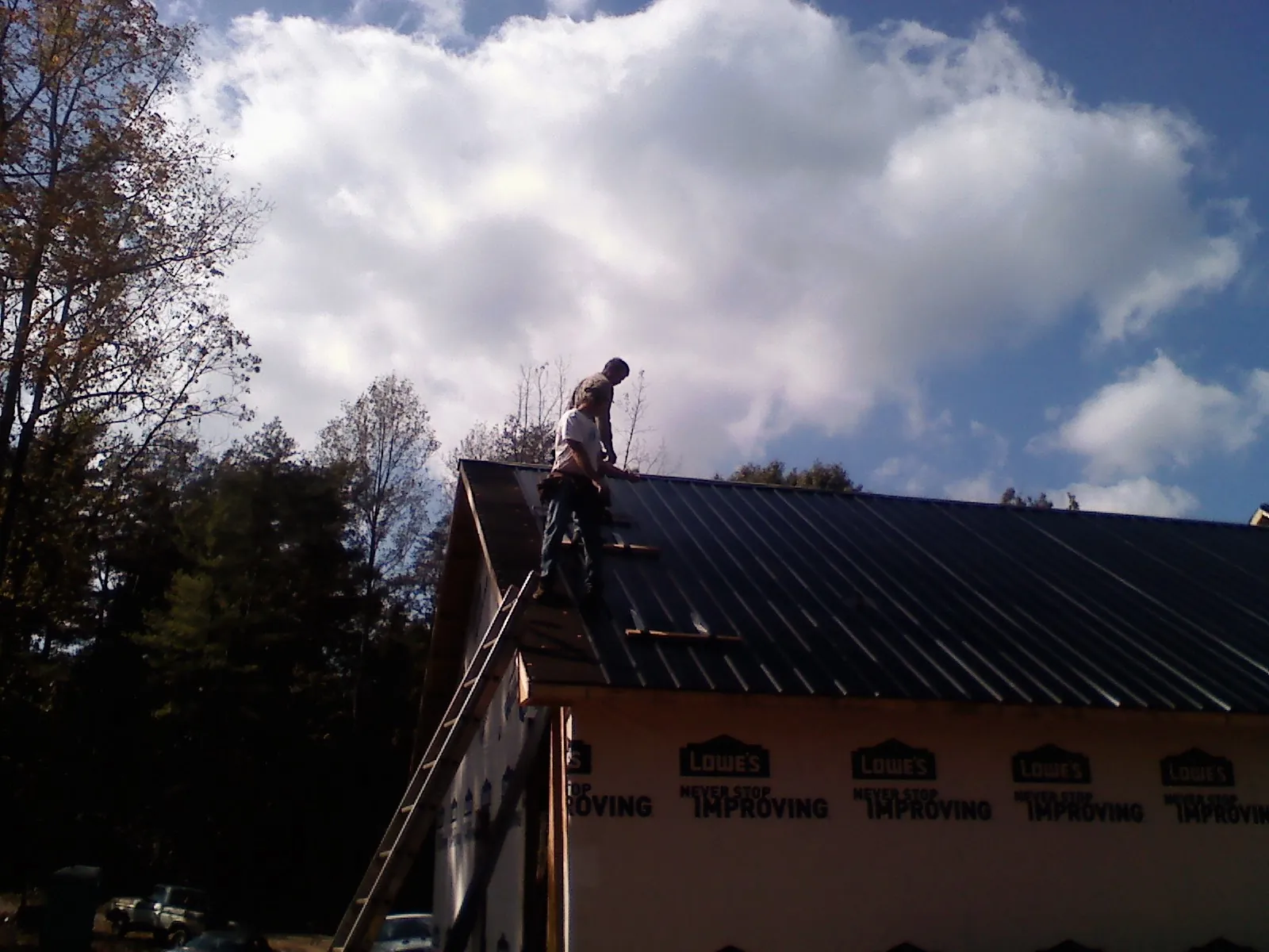 Roofer fastening dark metal panels high against a cloudy sky, from a Roof Inspection job in Hurricane Mills