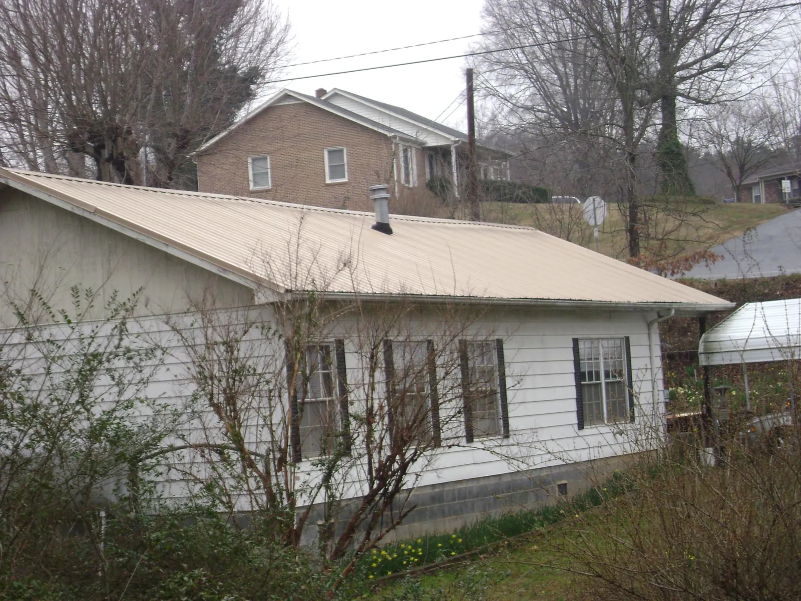 Tan metal roof on a white sided house set into a hillside — Commercial Roofing by Roofing Brothers in Hurricane Mills