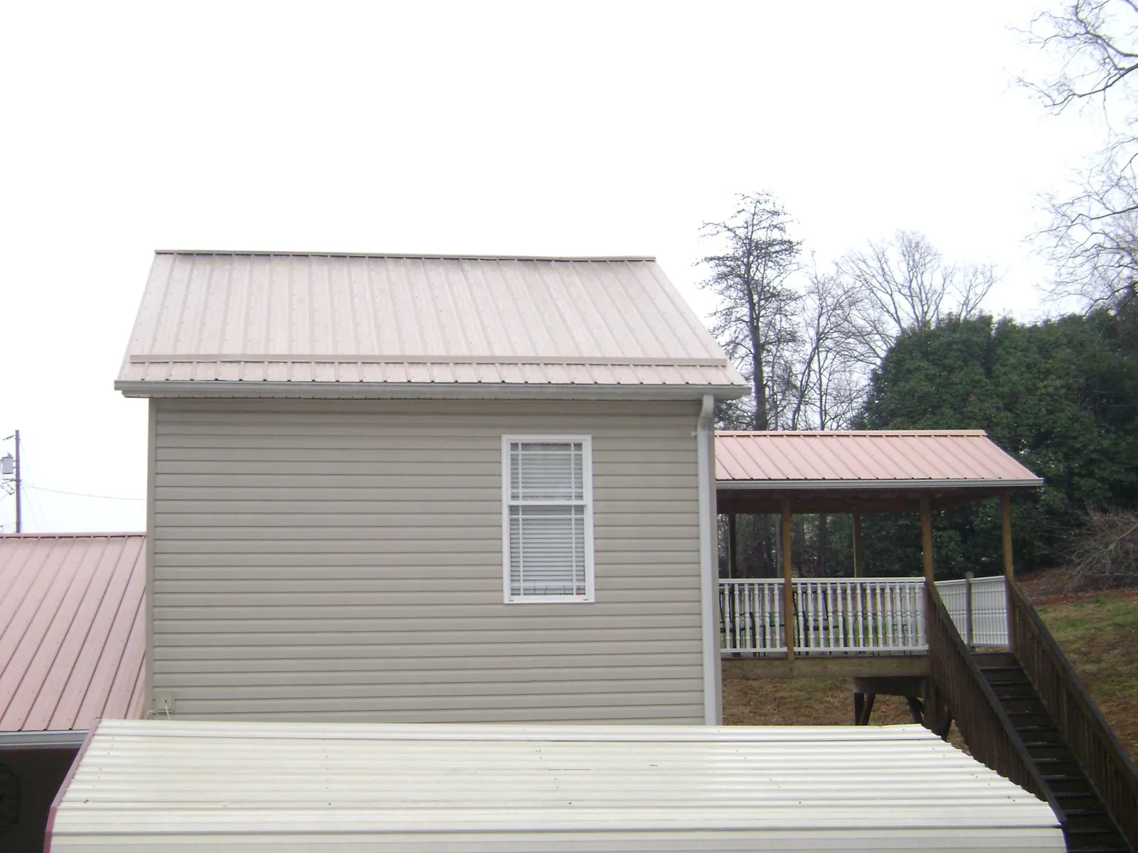 Tan metal roofs on a two story addition and attached porch, from a Roof Replacement job in Hurricane Mills
